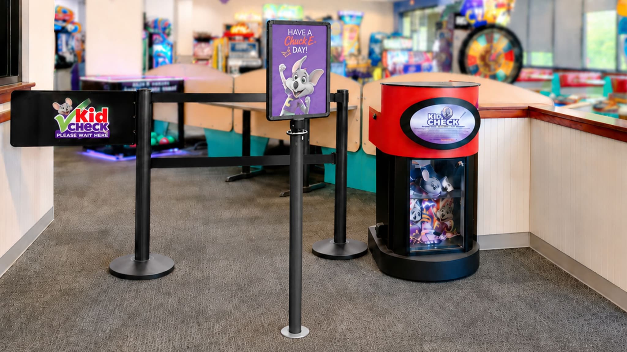 A Beltrac stanchion swing gate with a post-top sign marks the entry point at a Chuck E. Cheese kid check station.