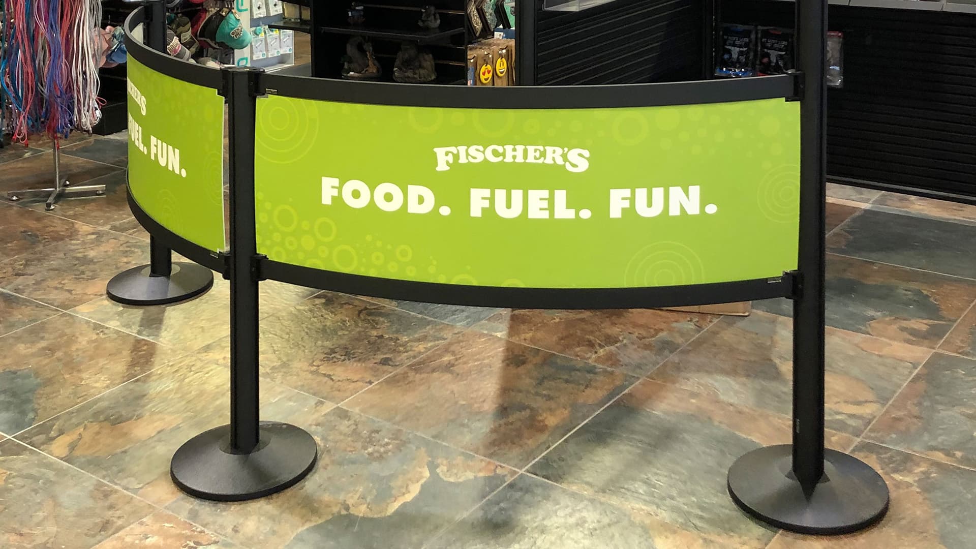 Rigid Rail barriers with Fischer's branded graphics form the checkout queue at a convenience store.