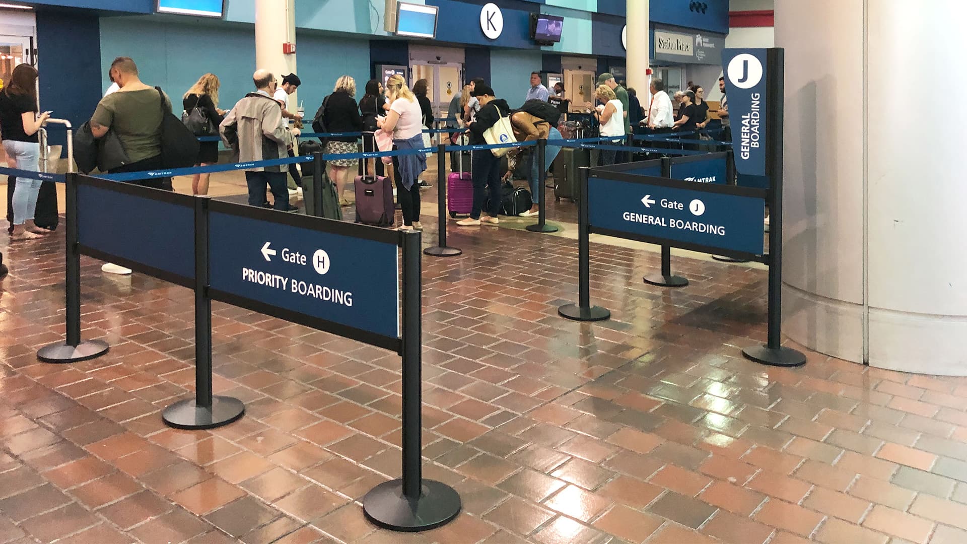 Rigid Rail barriers with printed wayfinding graphics guide passengers through the boarding queue at an Amtrak station.