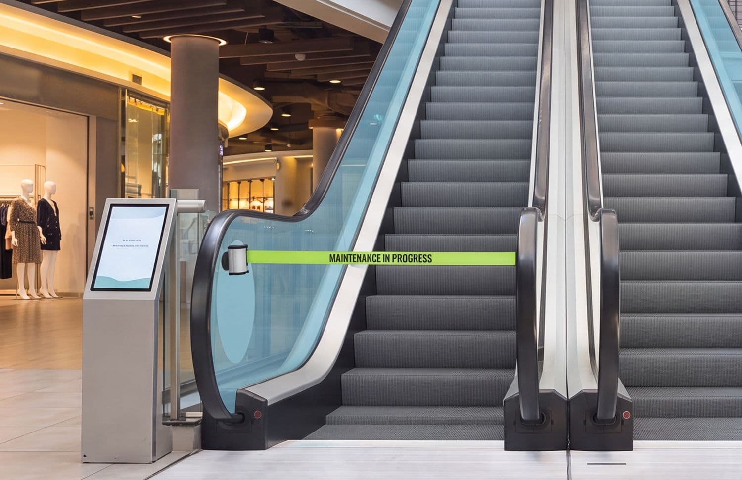 Glass-mount retractable belt safety barrier blocking an escalator entrance