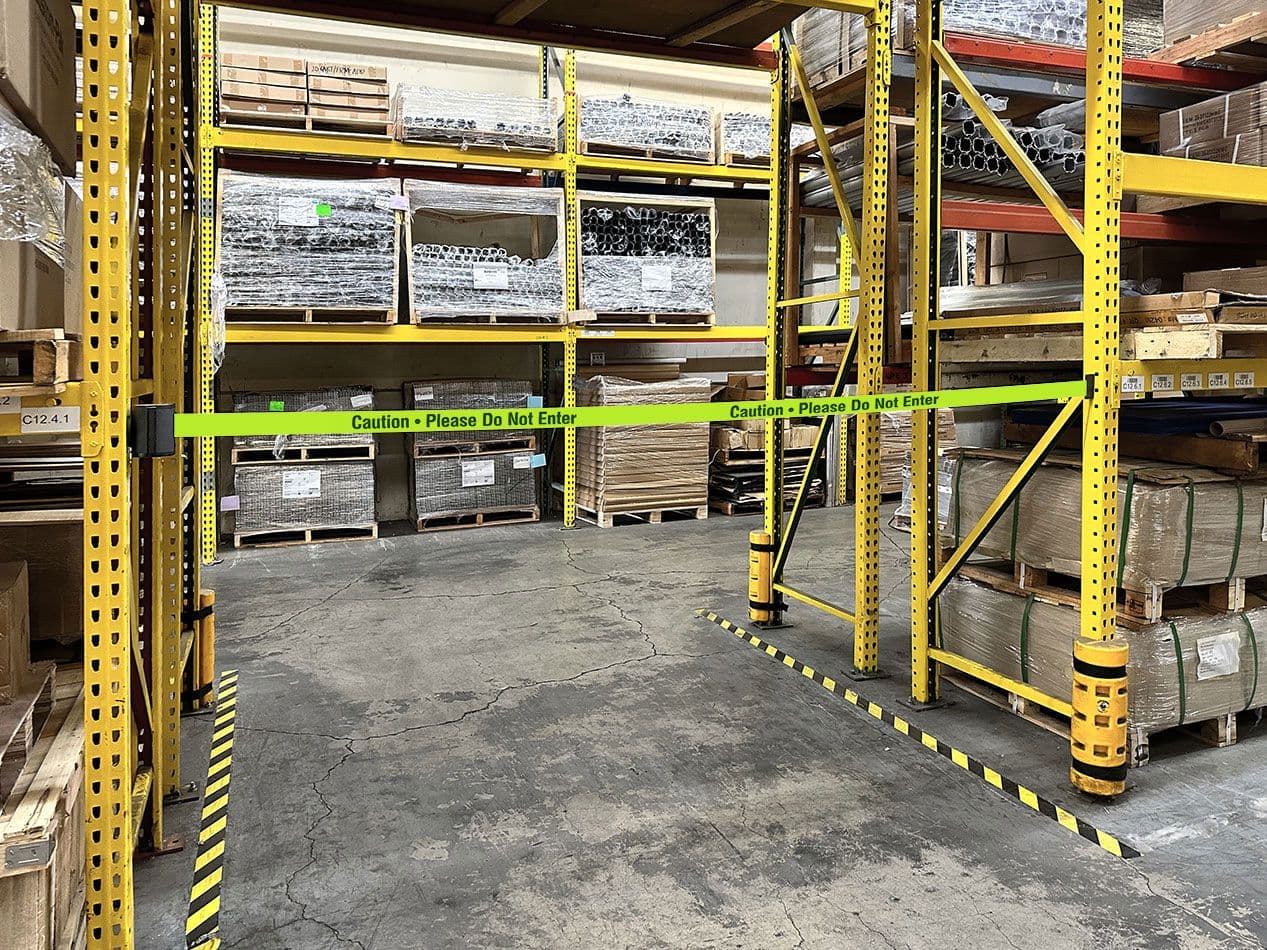 A magnetic retractable belt safety barrier attaches to rack uprights to close a warehouse aisle.