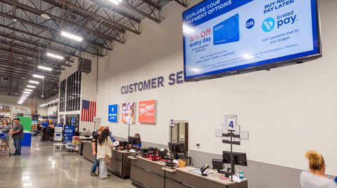 An electronic queuing system with LCD display and register lights at Academy Sports customer service desk.