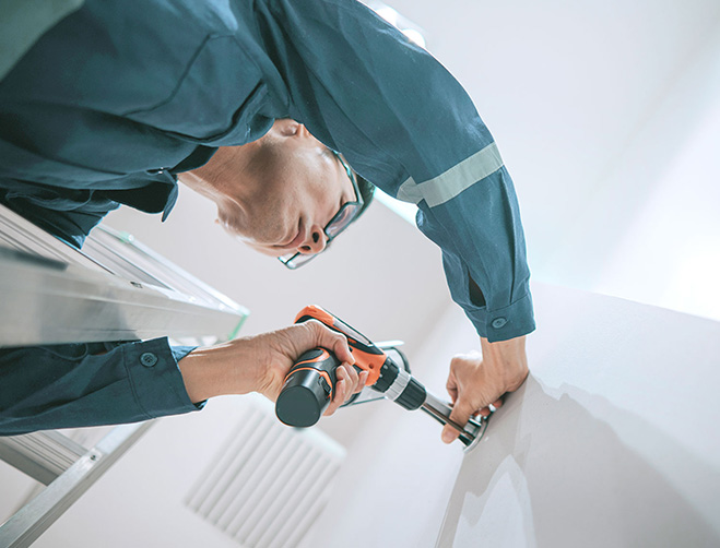 An installation technician drilling into a wall.